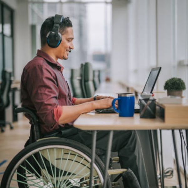 A wheelchair user working at a laptop in a bright office