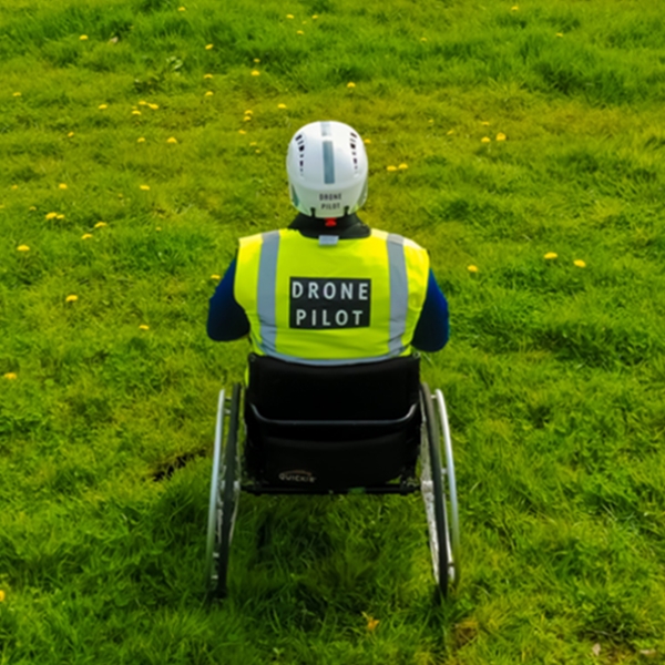 An SBS Foundation drone pilot flying from a wheelchair in a field